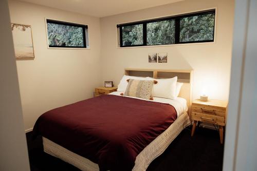 a bedroom with a bed and two windows at Kais Retreat in Punakaiki