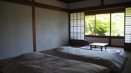 ein Zimmer mit zwei Betten, einem Tisch und Fenstern in der Unterkunft guesthouse waku in Nagiso
