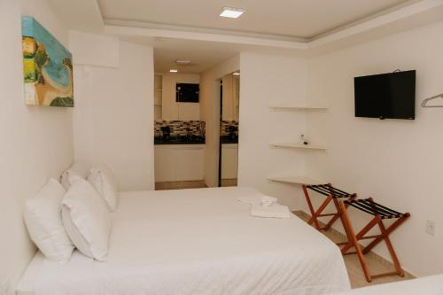 a white bedroom with a bed and a television at Pousada Areias do Pero in Cabo Frio