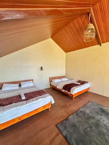 two beds in a room with wooden ceilings at Zambrud Villa Dieng in Kejajar