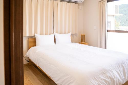 a bedroom with a large white bed with a window at Umibe no yado yo-riyo-ri in Amami