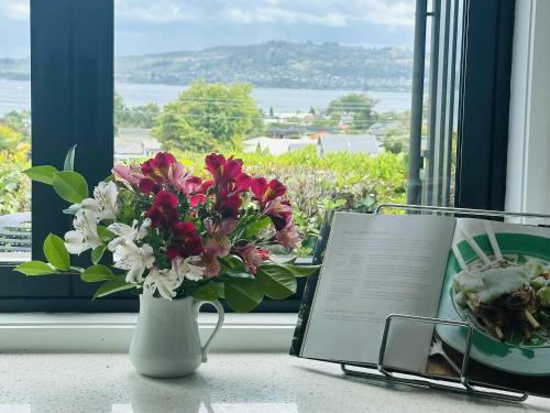 a vase with flowers and a book next to a window at Iconic Taupō Views in Taupo