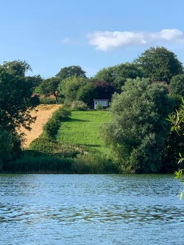 a house on a hill next to a body of water at Shepherd's Hut With Lake View In Ollerup in Vester-Skerninge