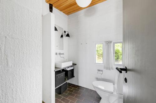 a white bathroom with a toilet and a sink at Architect Designed Holiday Home With Sea View in Gudhjem