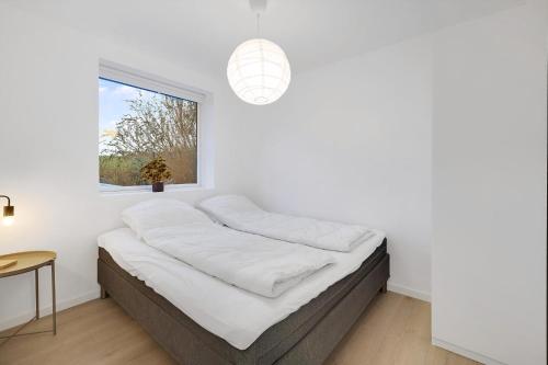 ein Bett in einem weißen Zimmer mit einem Fenster in der Unterkunft Schönes Neu Renoviertes Sommerhaus Am Meer in Frørup