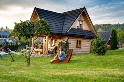 a woman sitting on a bench in front of a house at Pocztówka z Mizernej, drewniane domki, widok na Tatry, blisko Velo Czorsztyn, Jezioro Czorsztyńskie, rowery, spokojna okolica in Kluszkowce