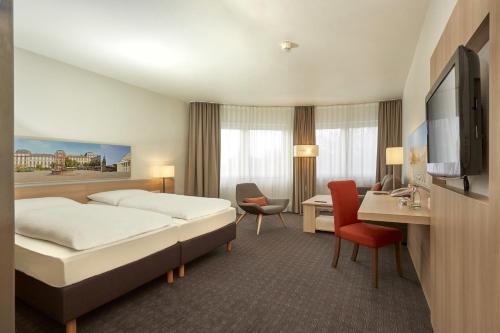 a hotel room with a bed and a desk and a tv at H+ Hotel Darmstadt in Darmstadt