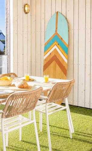 a table with two chairs and a surfboard leaned against a wall at Appart'Hôtel & Spa "Les Voiles" Belle Île en Mer in Carnac