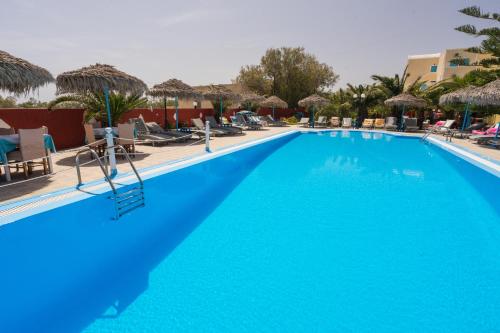 a large blue swimming pool with chairs and umbrellas at Almond Deluxe Suite in Santorini