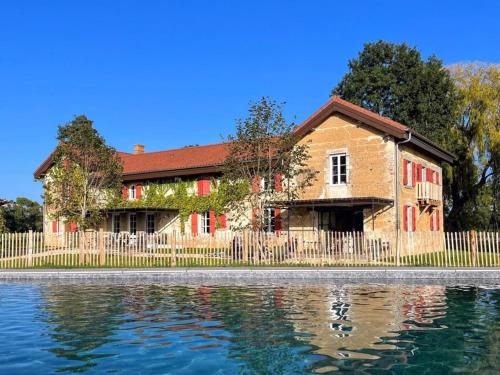 a house with a fence next to a body of water at La Ferme du Domaine de Bassol – Piscine & Billard in Mézériat