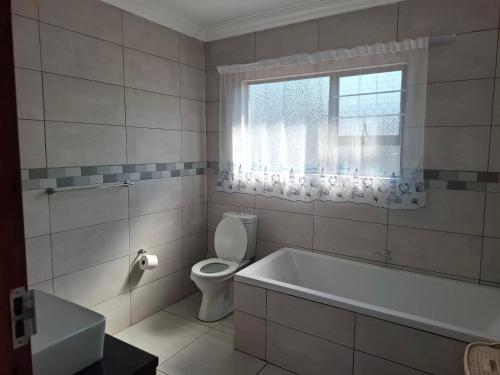 a bathroom with a tub and a toilet and a window at CE Guesthouse in Vanderbijlpark