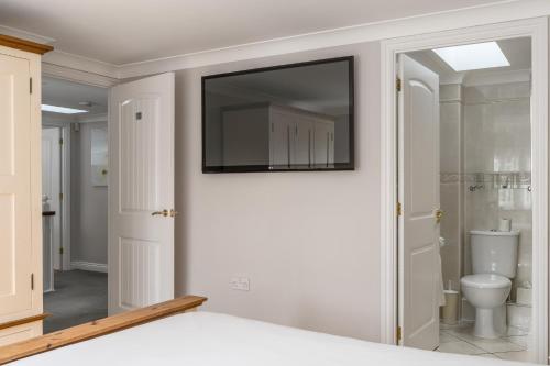 a bathroom with a toilet and a television on the wall at Finest Retreats - Hollies Coach House in Martock