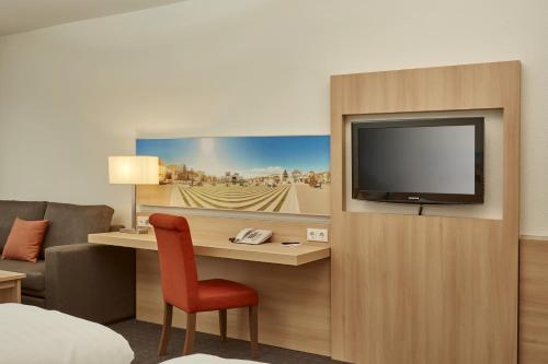 Habitación de hotel con TV y silla en H+ Hotel Darmstadt en Darmstadt
