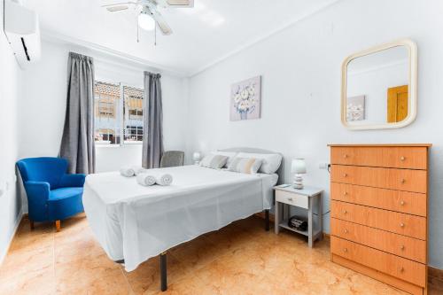 a white bedroom with a bed and a blue chair at Villa Patrick in Torrevieja