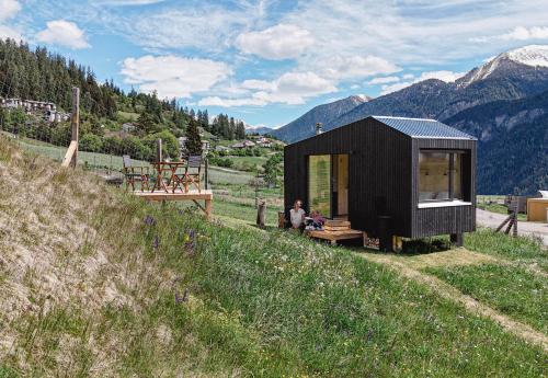 a black tiny house on a hill with a person sitting on a bench at Unbound Hütte Lenzerheide in Tiefencastel