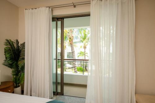 a bedroom with a window with white curtains at Chic poolside haven 3BR steps from the beach in Cap Malheureux