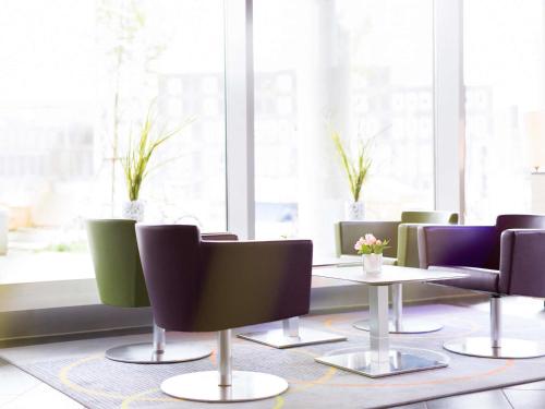 a dining room with tables and chairs and windows at Novotel Suites Hannover in Hannover