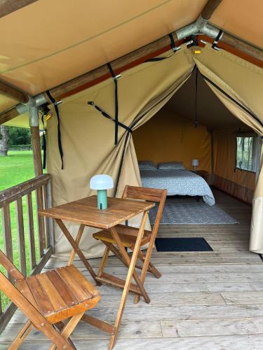 a tent with a bed and a table and chairs at Camping du pont d'Oust in Peillac