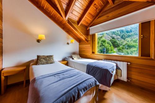two beds in a room with a large window at Del Sauco Apart & Spa in San Martín de los Andes
