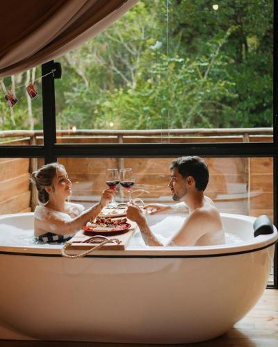 a man and woman sitting in a bath tub with wine glasses at chalé Platanus in Campos do Jordão