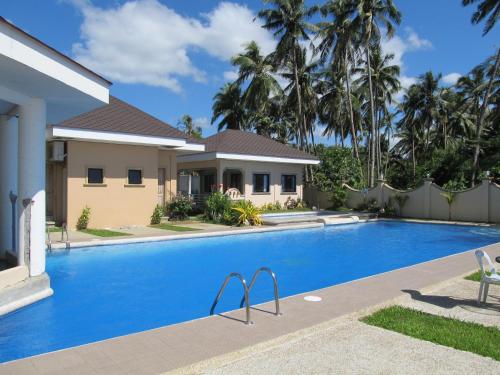 a swimming pool in front of a house with palm trees at Ucoy Beach Resort in Libertad