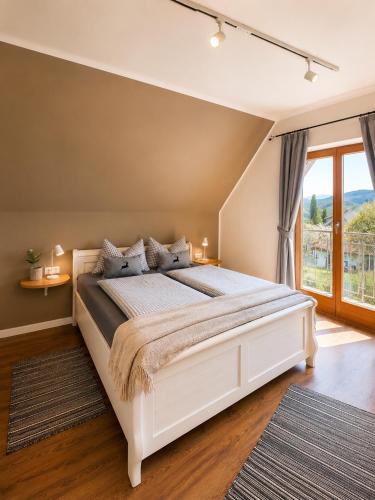 a bedroom with a white bed and a large window at EulenNest - Ferienhaus in Seeboden am Millstätter See mit Bergblick & Sauna in Seeboden