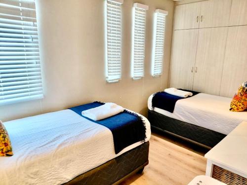 two beds in a room with white walls and windows at The Lazy Expat - Paarl - Self Catering Apartment in Paarl