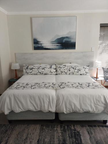 a bedroom with a white bed with a painting on the wall at Pecan Tree Forest Studio B with Terrace in Stellenbosch