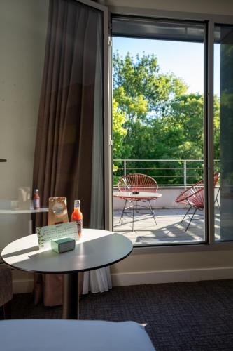 a room with a balcony with a table and a glass door at Best Western Plus Paris Meudon Ermitage in Meudon