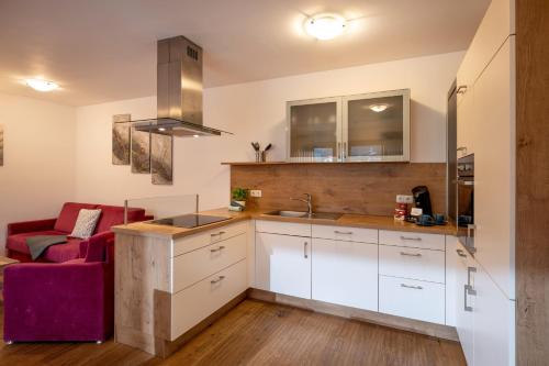 a kitchen with white cabinets and a red couch at Sonnplatzl Appartement Westendorf in Westendorf