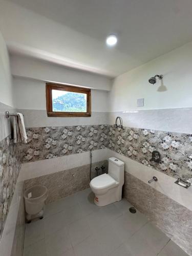 a bathroom with a toilet and a window at Crest Manali River View in Manāli