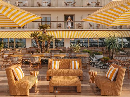a woman standing on the balcony of a hotel with chairs and umbrellas at Hôtel Les Brises in La Rochelle
