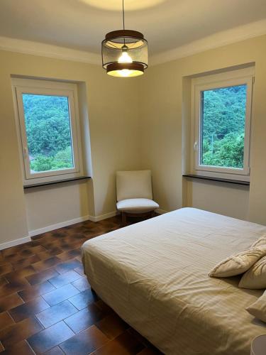 a bedroom with a bed and two windows and a chair at Casa Nina in Valbravenna