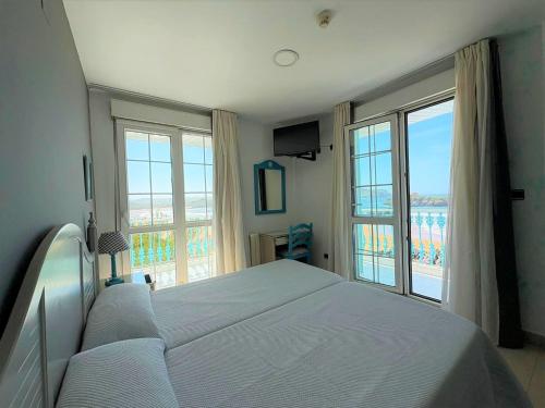 a bedroom with a large bed and large windows at Hotel Pineda Playa in Noja