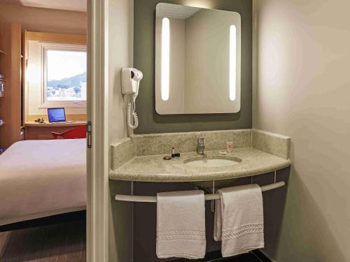 a bathroom with a sink with a mirror and a bed at ibis Jundiai Shopping in Jundiaí