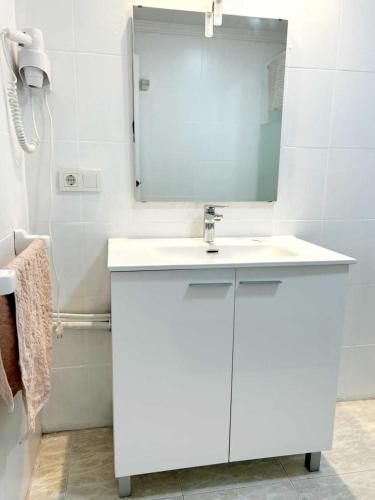 a white bathroom with a sink and a mirror at Pequeño estudio frente al mar, piscina y parking in Villajoyosa
