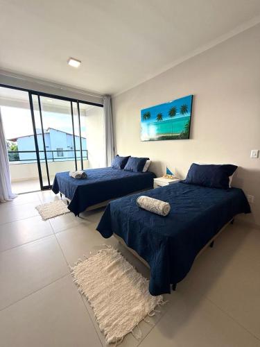 two beds in a bedroom with blue sheets and a window at Casa 03 suites Maragogi Japaratinga in Japaratinga