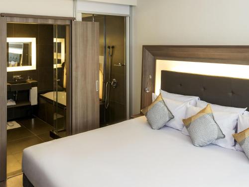 a bedroom with a large white bed and a bathroom at Novotel Santos Gonzaga in Santos