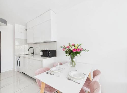 a white kitchen with a table and flowers in a vase at BelMare Seaside Apartment by Solarento in Międzyzdroje