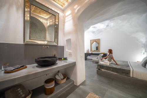 a woman sitting on a bed in a bedroom with a sink at Numa Santorini in Fira