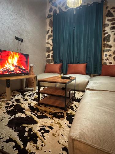 a living room with a fireplace and a couch and a tv at Chalet en Pierre Benslimane in Aïn Sferjila