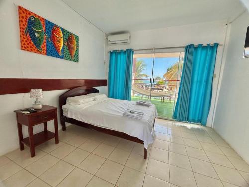 a bedroom with a bed and a window with blue curtains at Hotel Las Terrazas de Bonanza in Zorritos