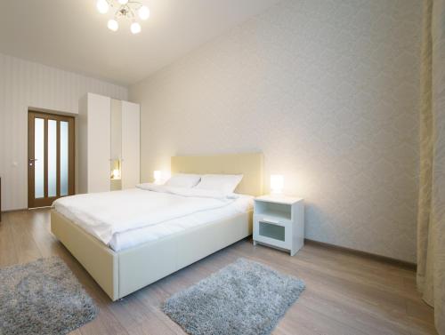 a white bedroom with a bed and a nightstand and two rugs at PaulMarie Apartments on Mayakovskogo 24 in Brest