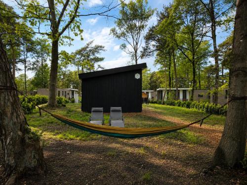 two chairs and a hammock in a park with trees at Colibri Huisje in Haarle