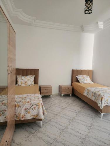 a bedroom with two beds and a white wall at F3 entre nature et calme in Raʼs al Jabal