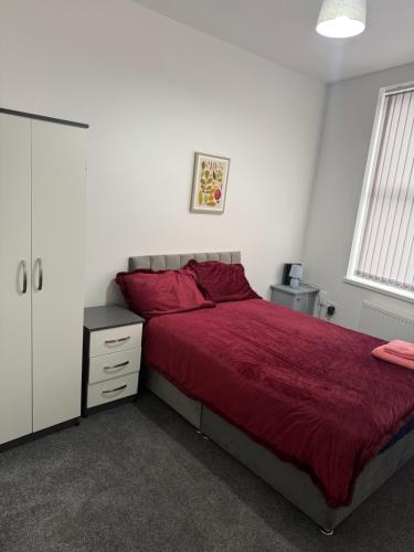 ein Schlafzimmer mit einem Bett mit roter Tagesdecke und einem Schrank in der Unterkunft PLUS Properties Dike 1 in Stoke on Trent