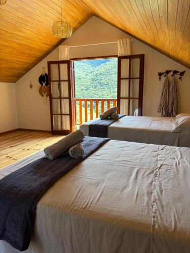 three beds in a room with a large window at Chalé Recanto da Grota in Passa Vinte