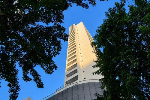 a tall white building with trees in the foreground at GRU Residence by Housi in Guarulhos
