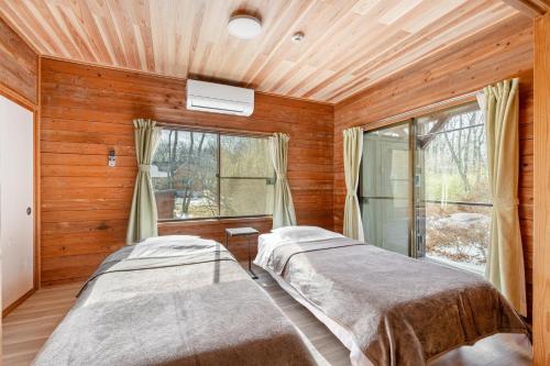 two beds in a room with wooden walls and windows at 那須ウッドペッカーBBQ & Petりんどう湖近くの一棟貸別荘 in Nasu