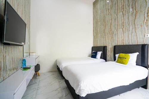 a bedroom with two beds and a flat screen tv at Urbanview Hotel Nimara Ngawi by RedDoorz in Ngawi